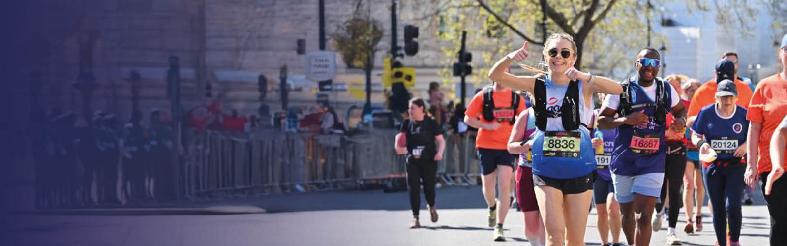 A young woman smiling with thumbs up, while running a marathon in an Age UK top