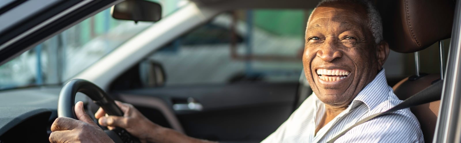 An older Black man driving a car, smiling
