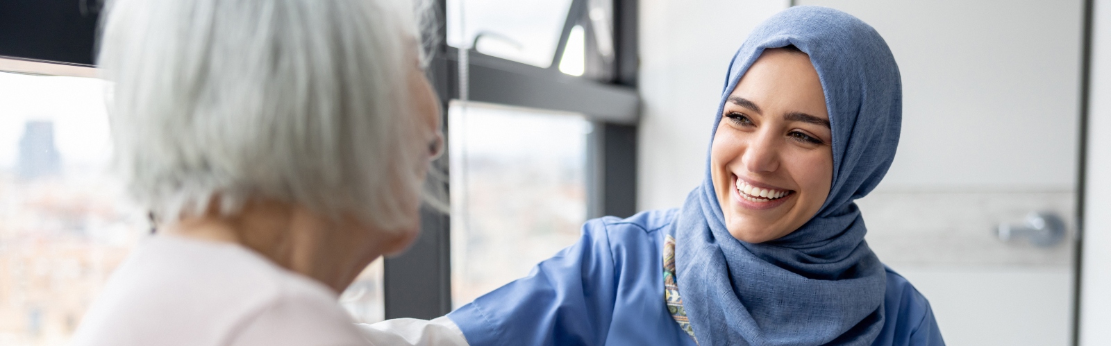 A young medical professional in a hijab, smiling at an older woman